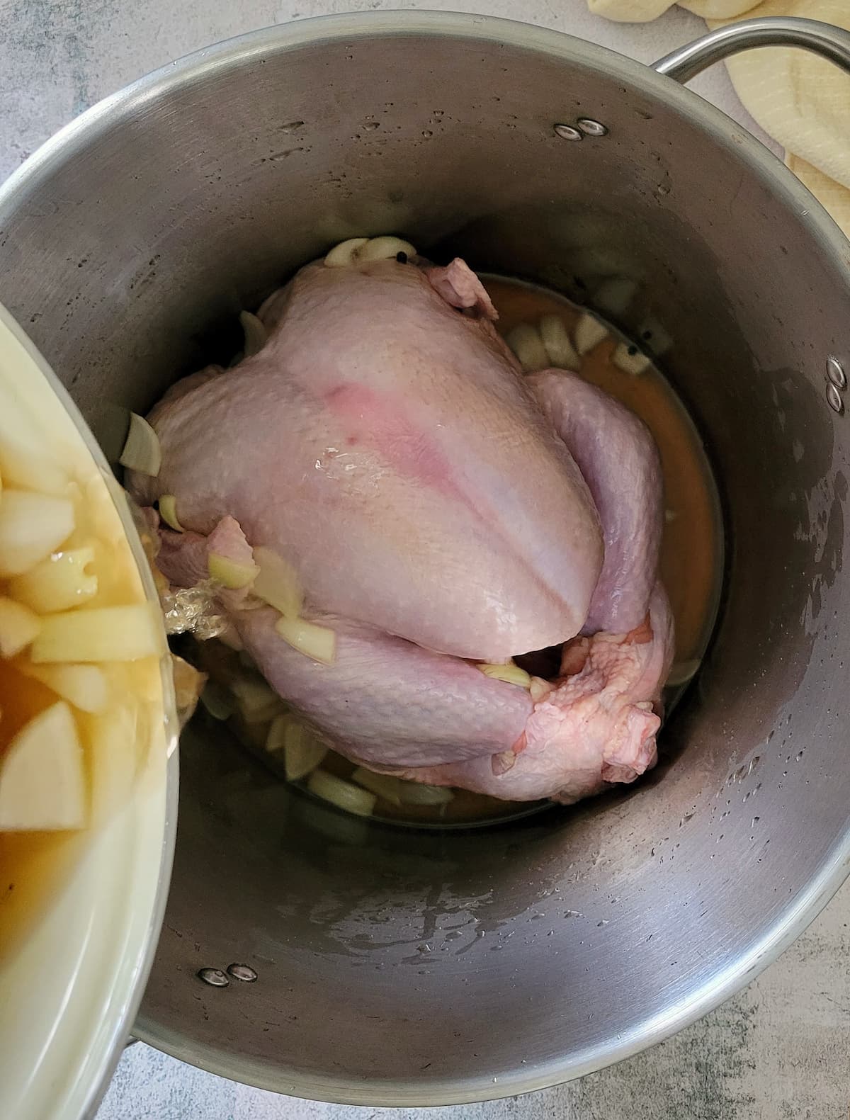 brine with chopped onions being poured on top of a raw turkey in a large pot