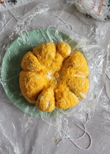 pumpkin shaped cheeseball on a plastic wrap lined plate.