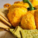 side view of pumpkin shaped cheese ball on a plate with crackers