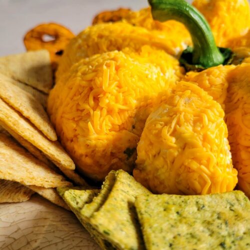 side view of pumpkin shaped cheese ball on a plate with crackers