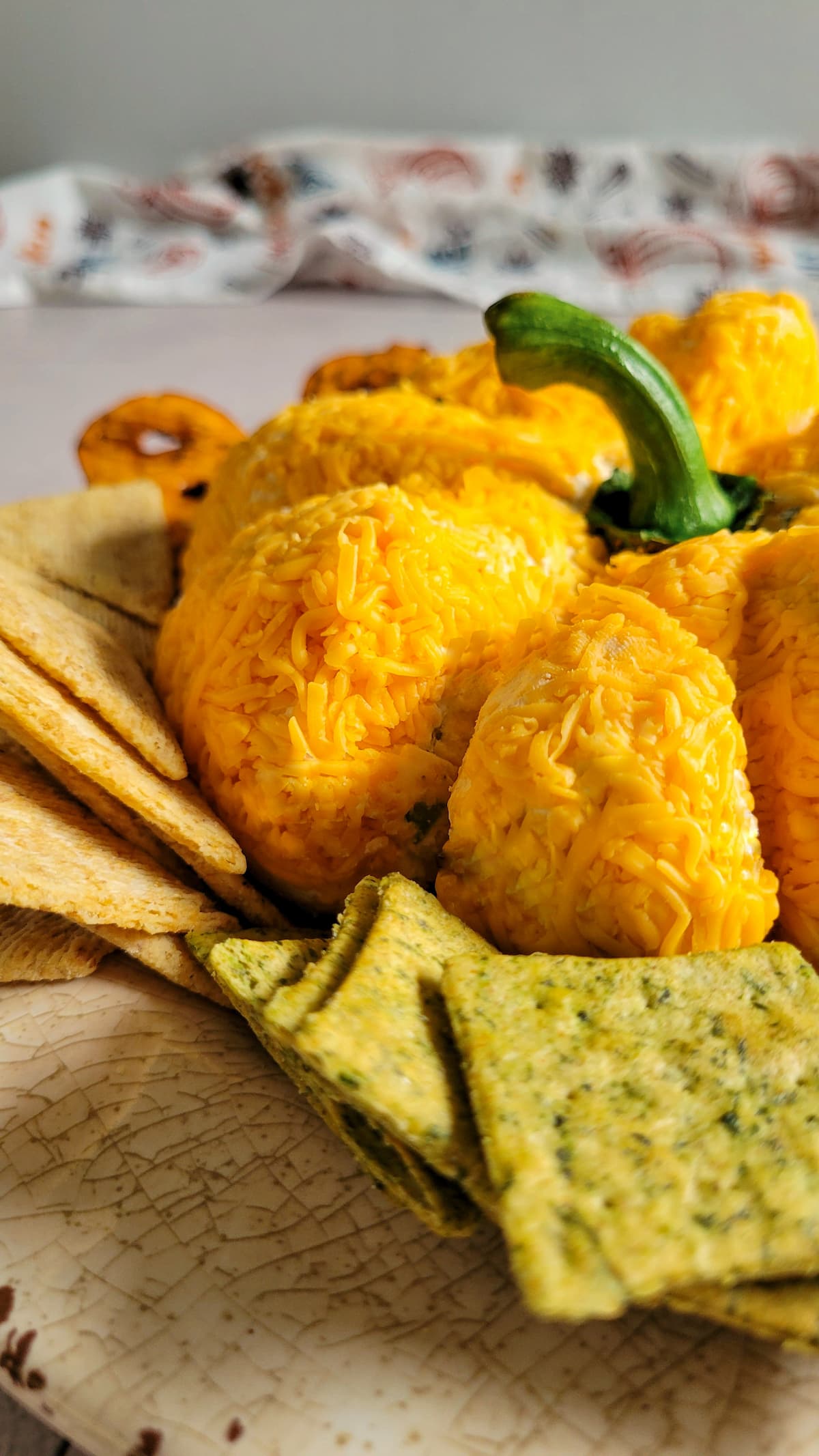 side view of pumpkin shaped cheese ball on a plate with crackers