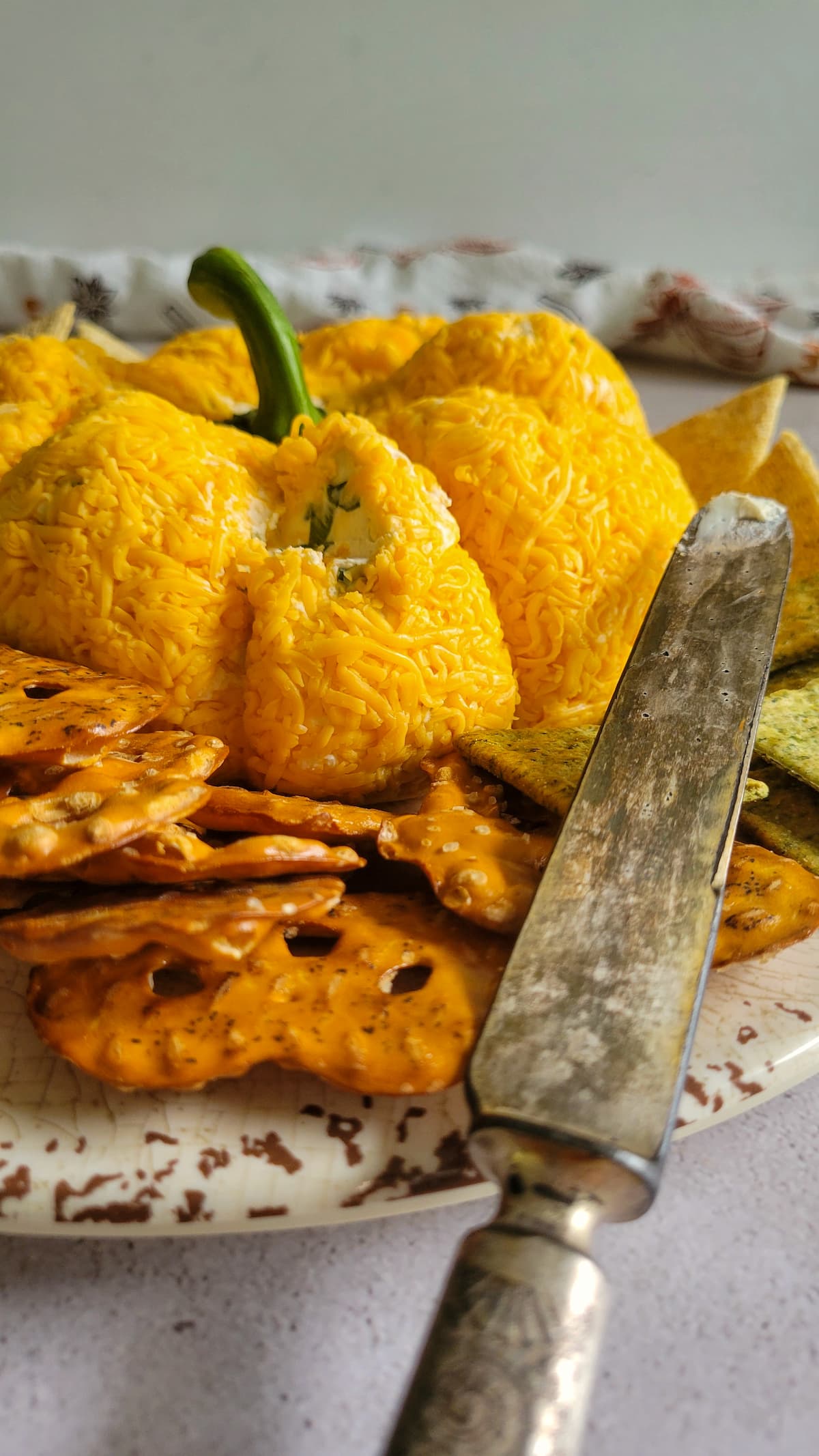 pumpkin shaped cheeseballs with crackers surrounding it, some missing onto a knife in frame