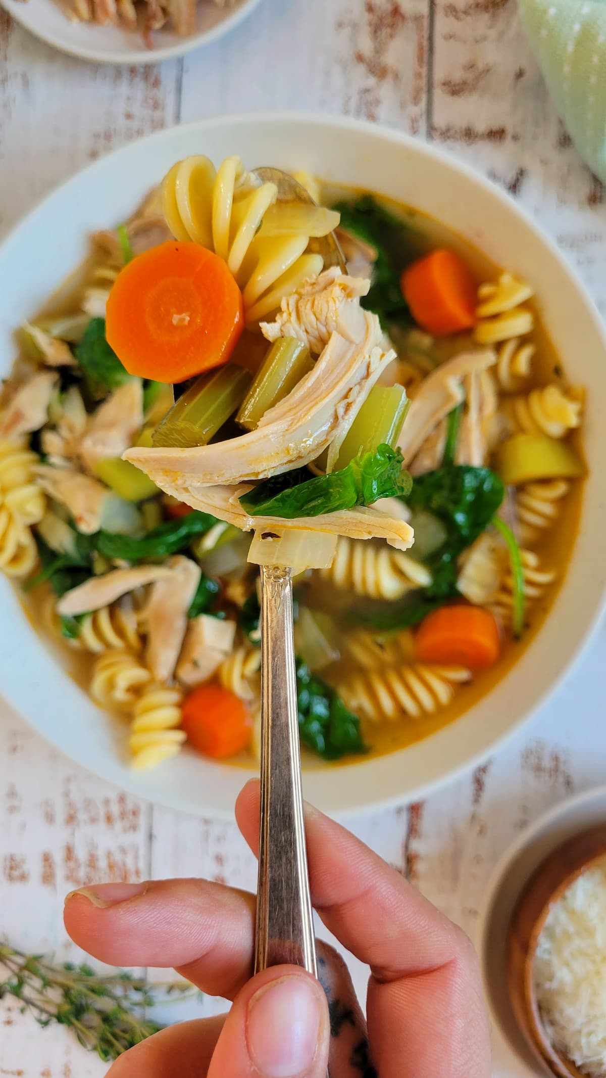 hand with a spoonful of veggies, turkey and pasta over a bowl of the rest of it