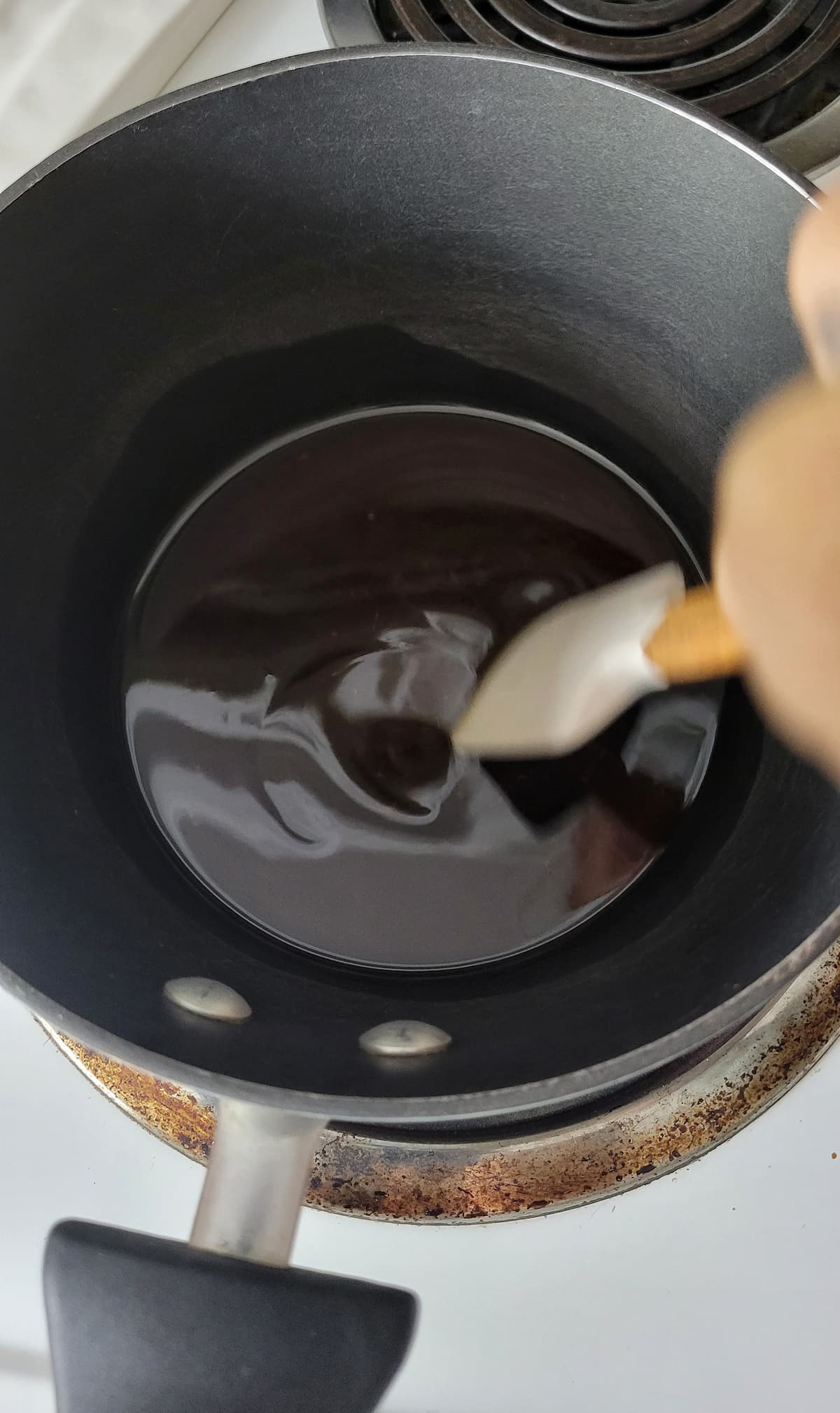 hand with a spatula stirring syrup in a pot on a burner