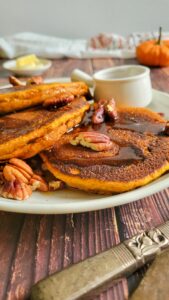 pumpkin pancakes, syrup, and toasted pecans on a plate.