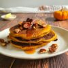 pancakes stacked on a plate with syrup and pecans
