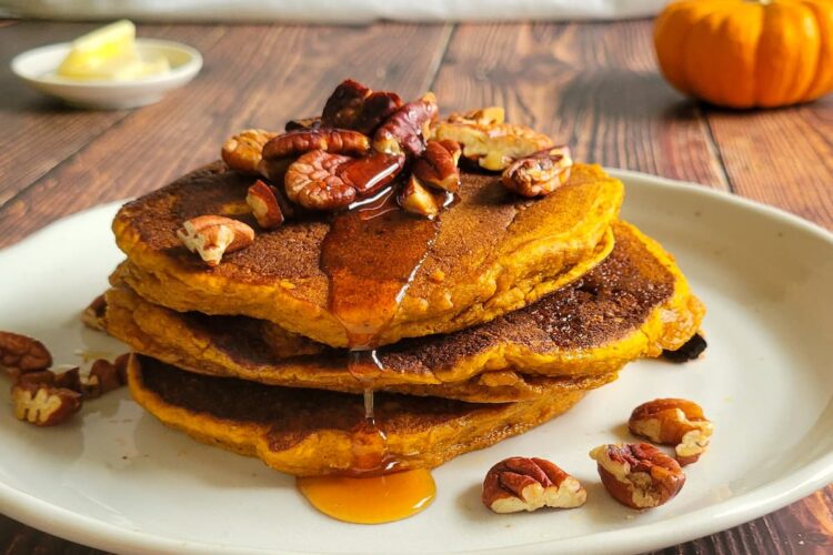 pancakes stacked on a plate with syrup and pecans