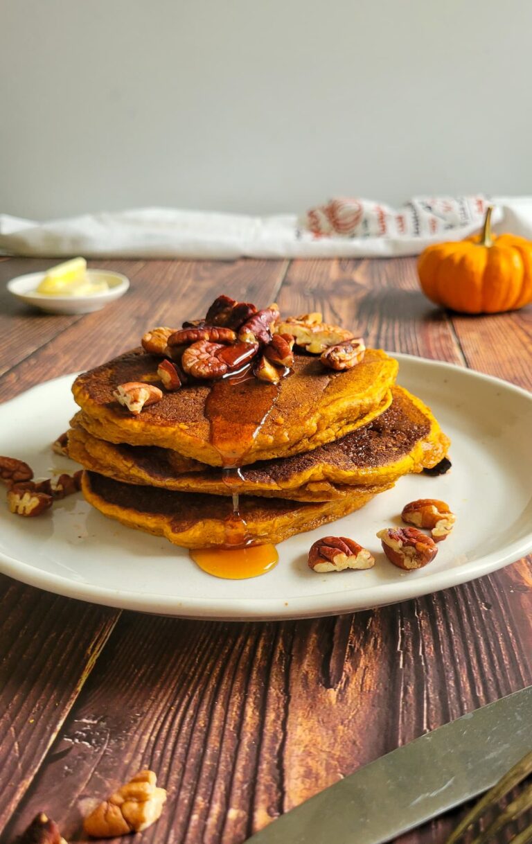 pancakes stacked on a plate with syrup and pecans