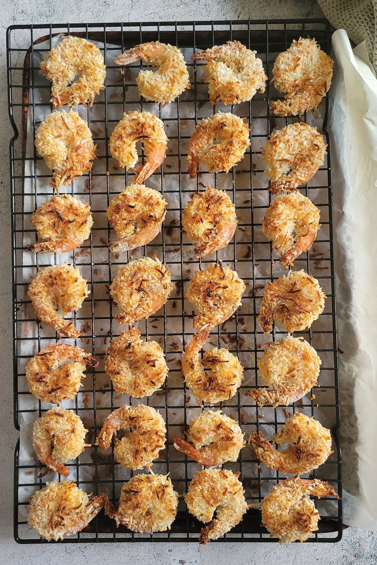baked coconut shrimp on a wire rack over a parchment lined baking sheet