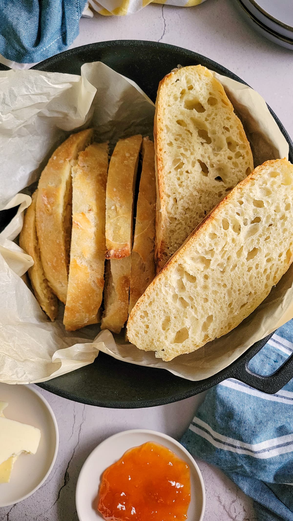 sliced bread in a parchment lined dutch oven, jam and butter on the side