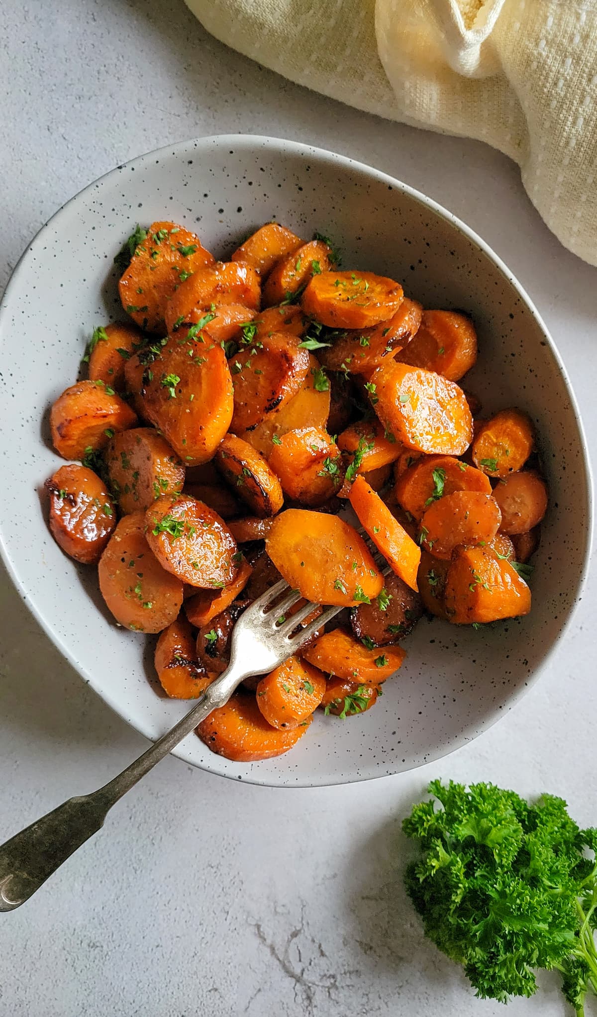 sliced glazed carrots in a bowl with chopped fresh parsley, fork in the bowl