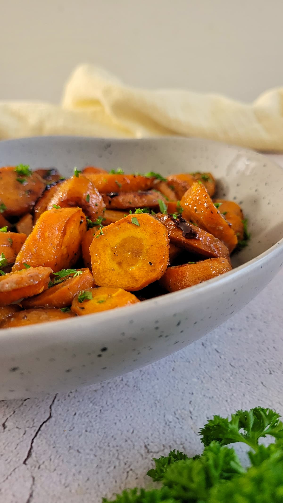 side view of sliced glazed carrots garnished with chopped fresh parsley in a bowl