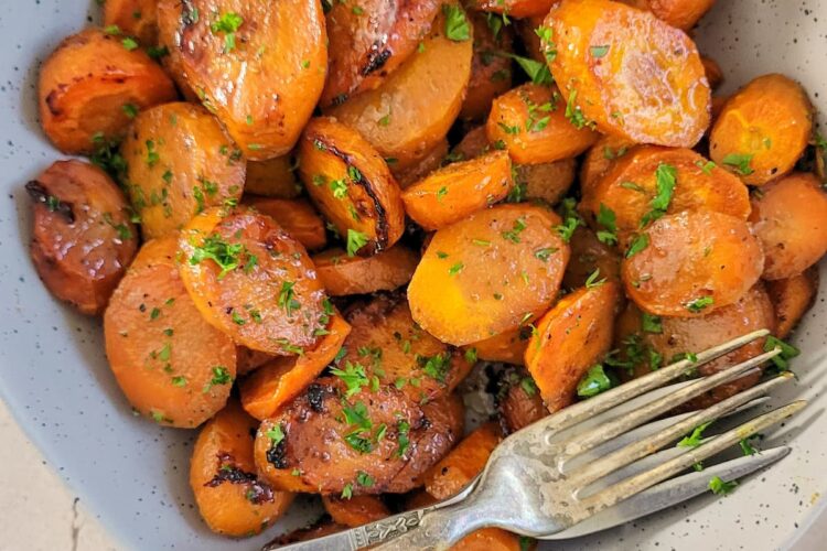 sliced glazed carrots garnished with fresh chopped parsley in a bowl