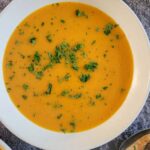 bowl of carrot soup garnished with chopped fresh parsley next to a few spoons