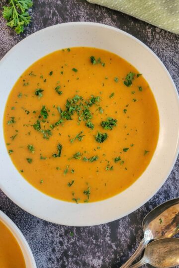 bowl of carrot soup garnished with chopped fresh parsley next to a few spoons