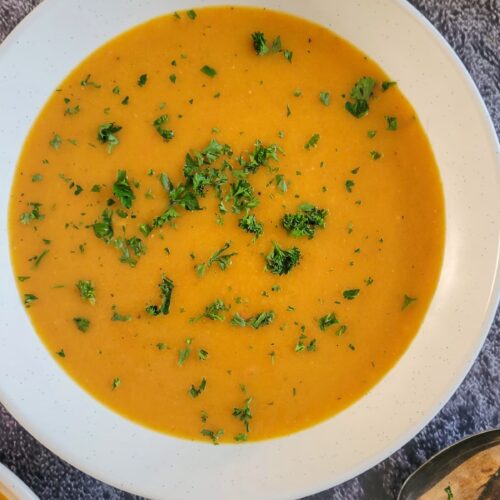bowl of carrot soup garnished with chopped fresh parsley next to a few spoons