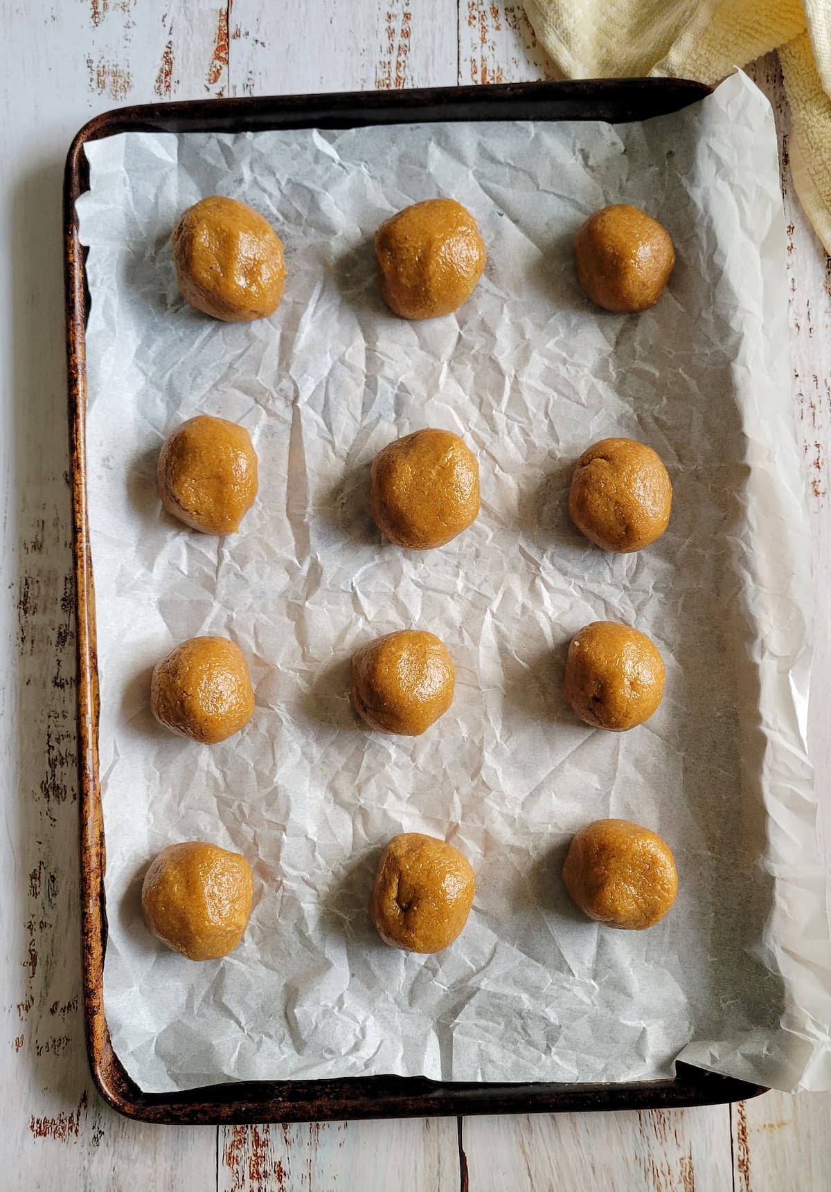 12 balls of cookie dough spread out evenly on a parchment lined baking sheet