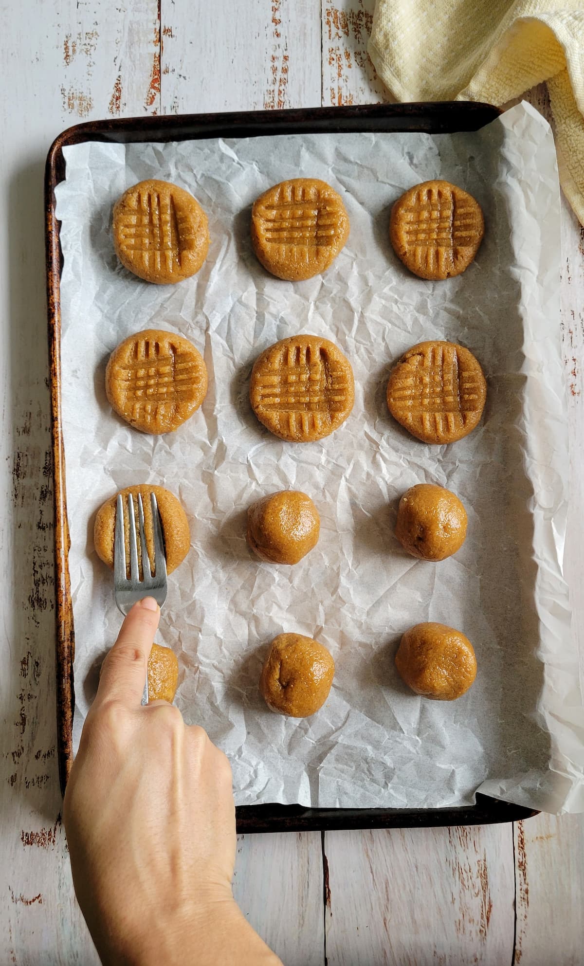 unbaked cookies on a parchment lined baking sheet, half pressed down and half in balls, hand pressing one down with a fork