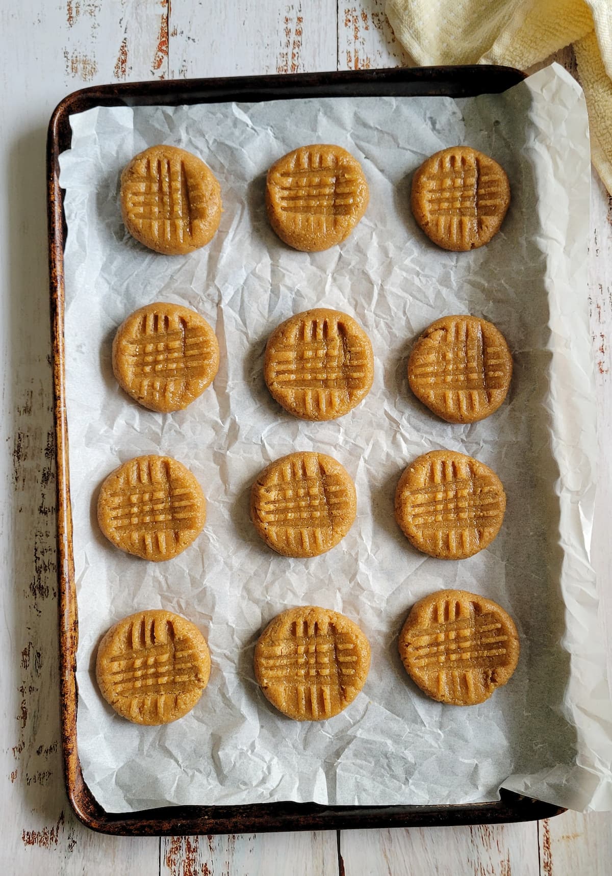 unbaked peanut butter cookies with a criss cross pattern on a parchment lined baking sheet
