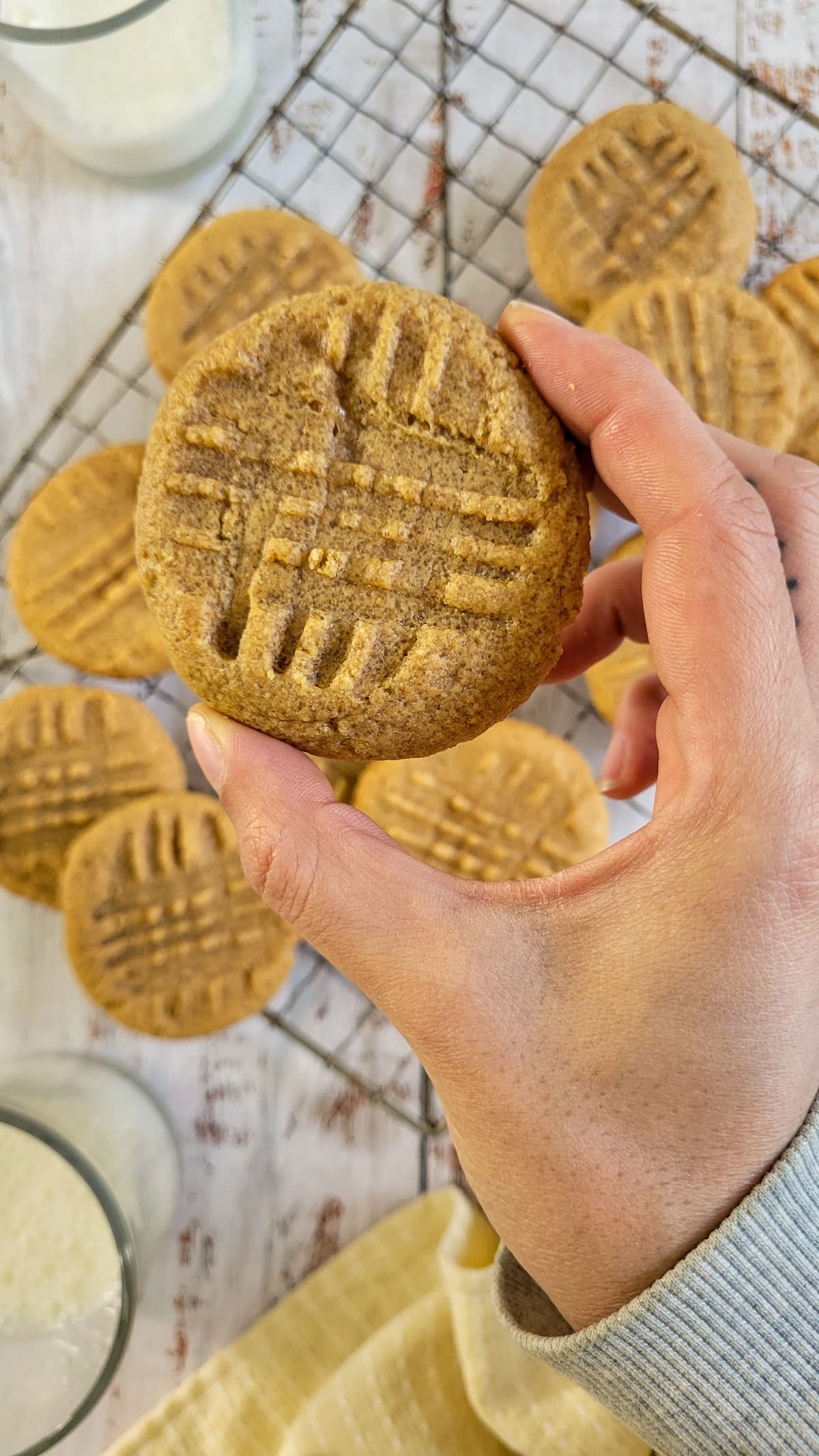 hand holding a peanut butter cookie over a wire rack with more