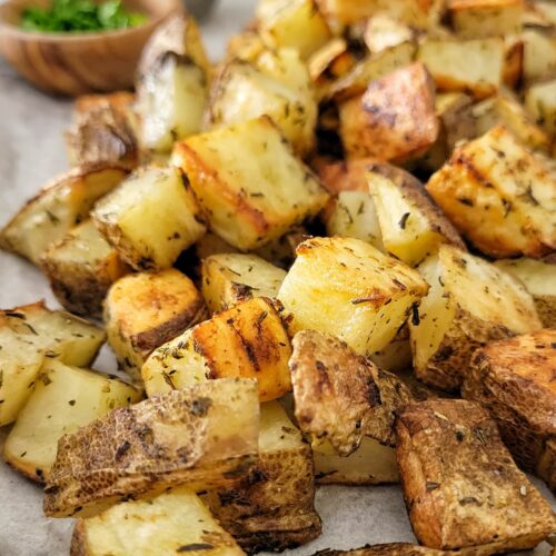 crispy seasoned home fries on a parchment lined baking sheet, ramekin of fresh chopped parsley and ketchup in the background
