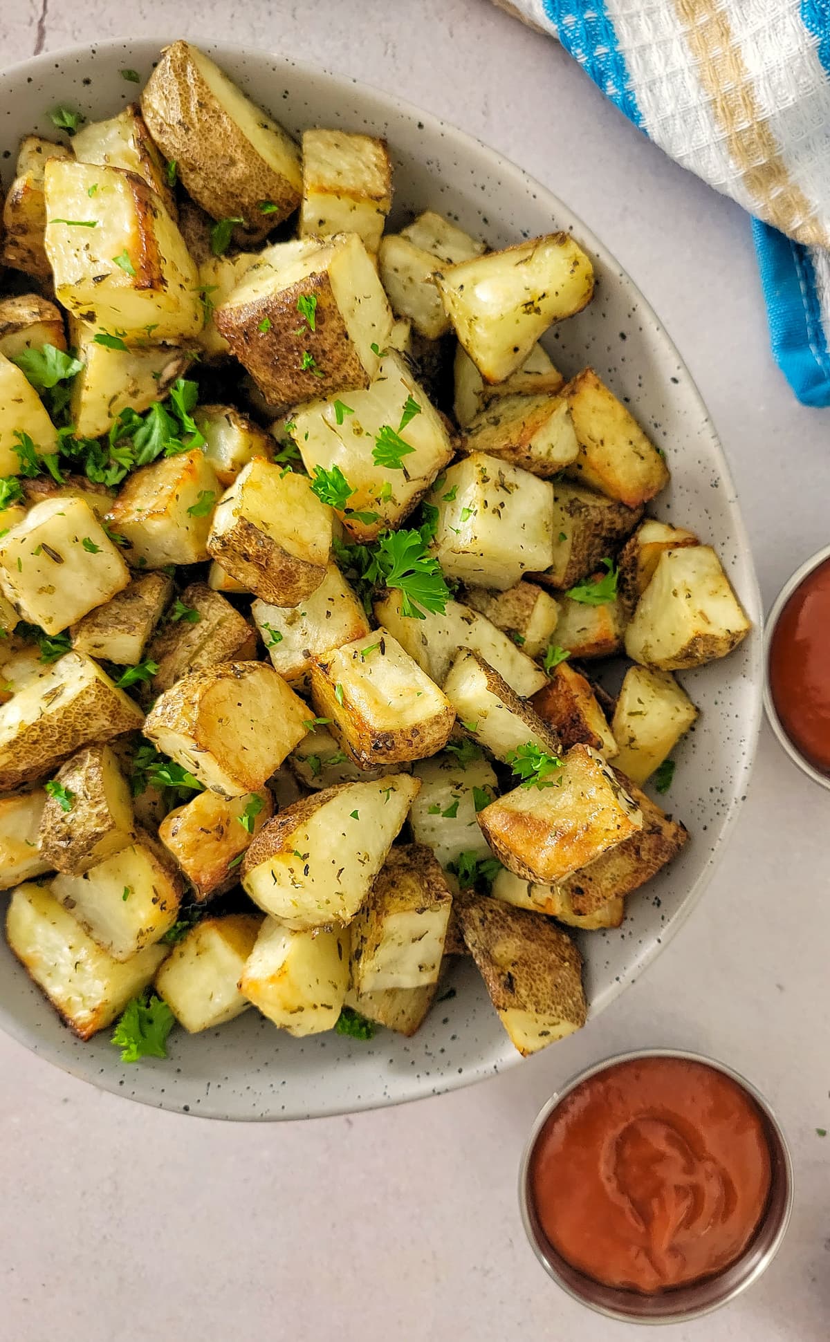 bowl of home fries with fresh chopped parsley, ramekins of ketchup in the background