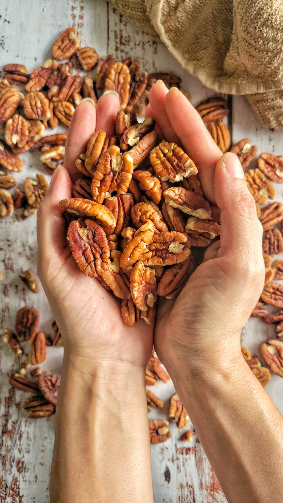 hands holding pecans over a surface with more of them