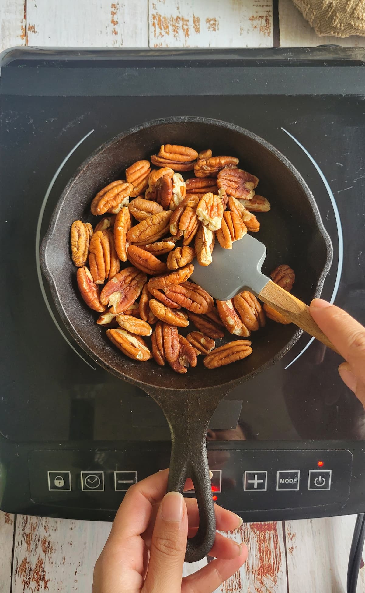 hand with a small rubber spatula stirring pecans in a small skillet on a burner