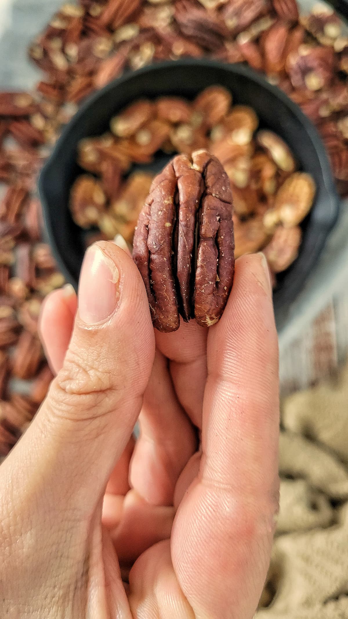hand holding a pecan over a skillet and sheet pan with more