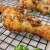 chicken drumsticks garnished with fresh parmesan cheese and parsley on a wire rack on a parchment lined baking sheet