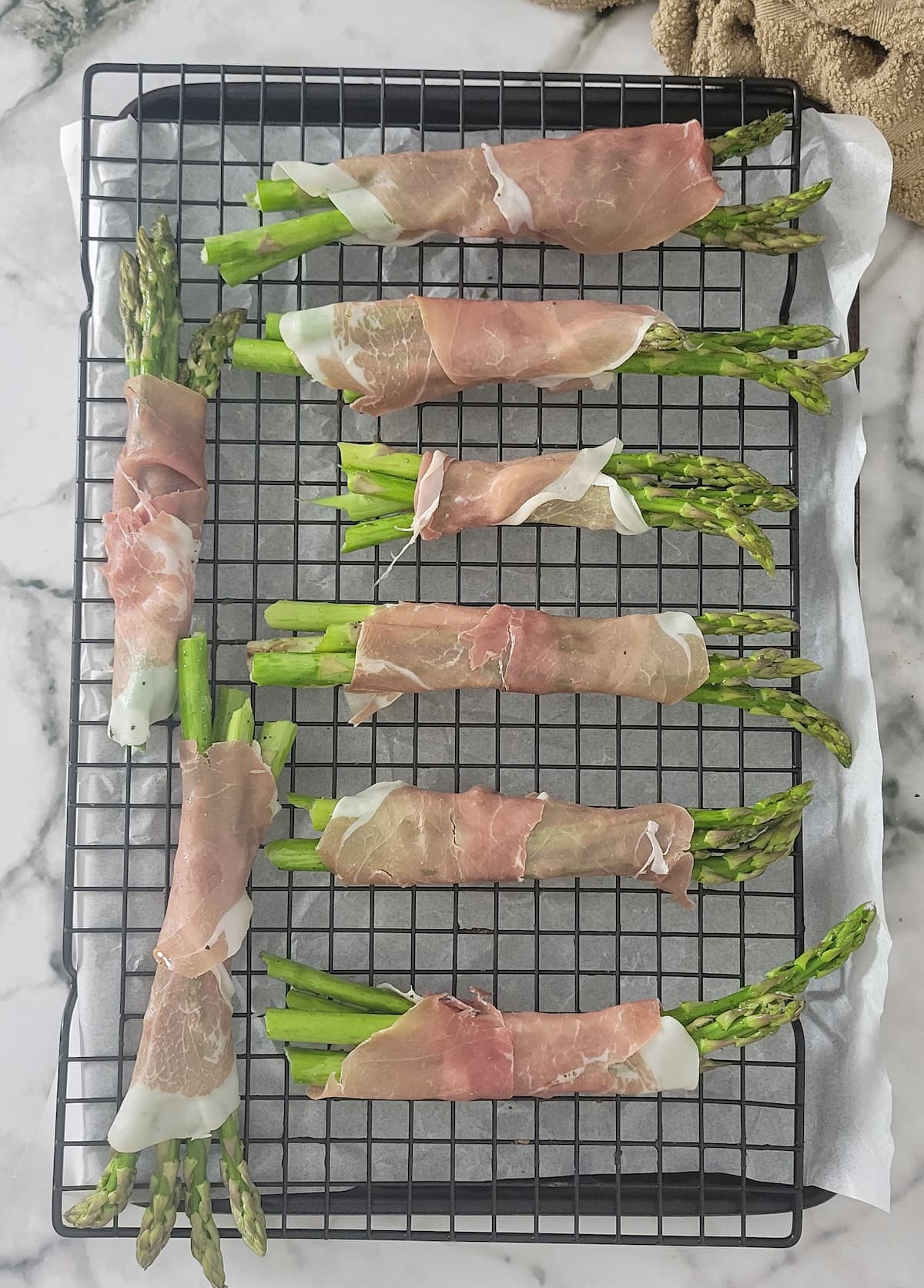 prosciutto wrapped asparagus bundles on a wire rack over a parchment lined baking sheet