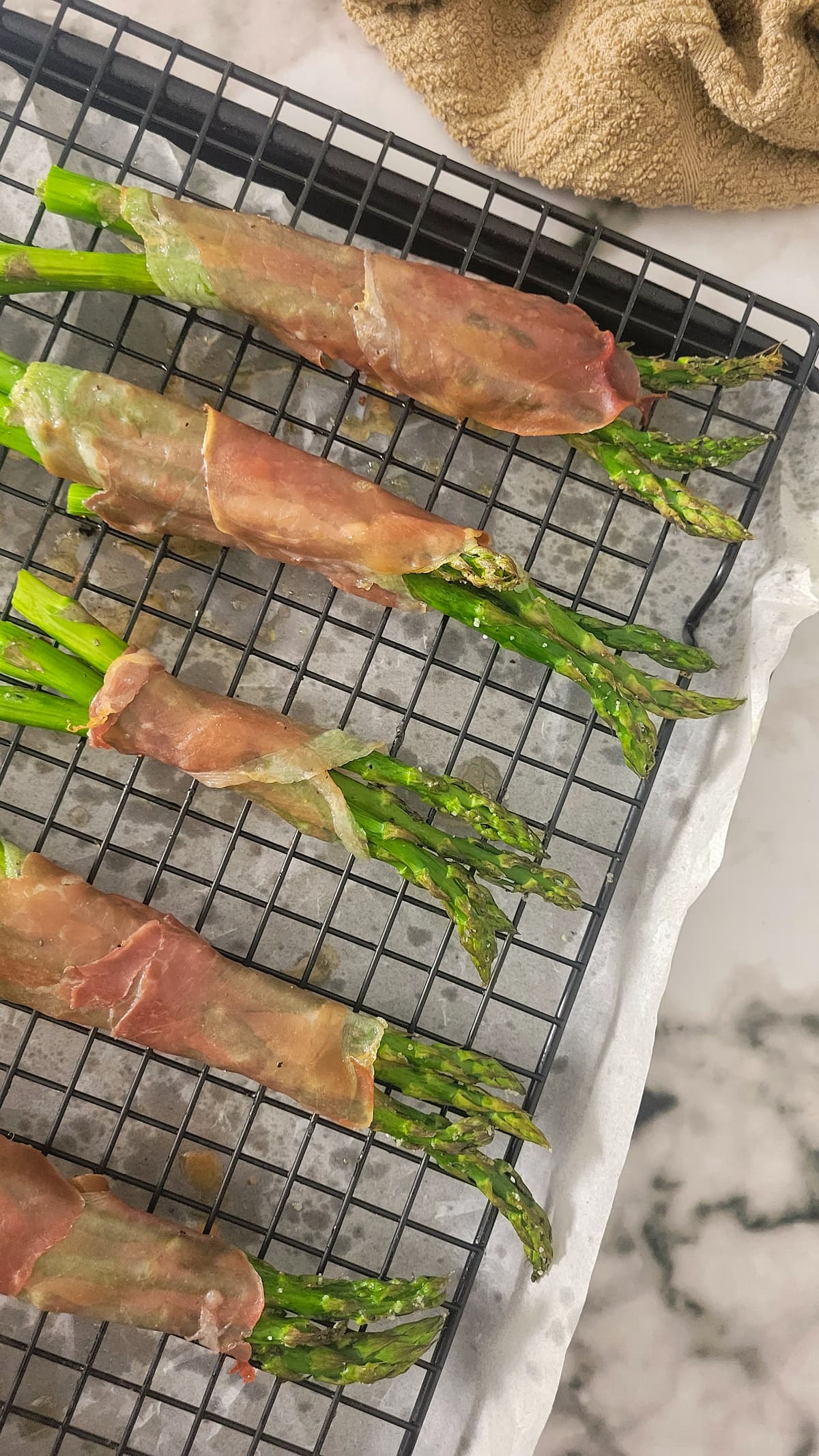 bundles of asparagus wrapped in prosciutto on a wire rack over a parchment lined baking sheet