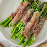 prosciutto wrapped asparagus bundles on a plate garnished with fresh grated parmesan cheese