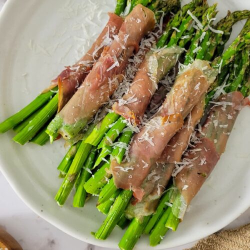 prosciutto wrapped asparagus bundles on a plate garnished with fresh grated parmesan cheese