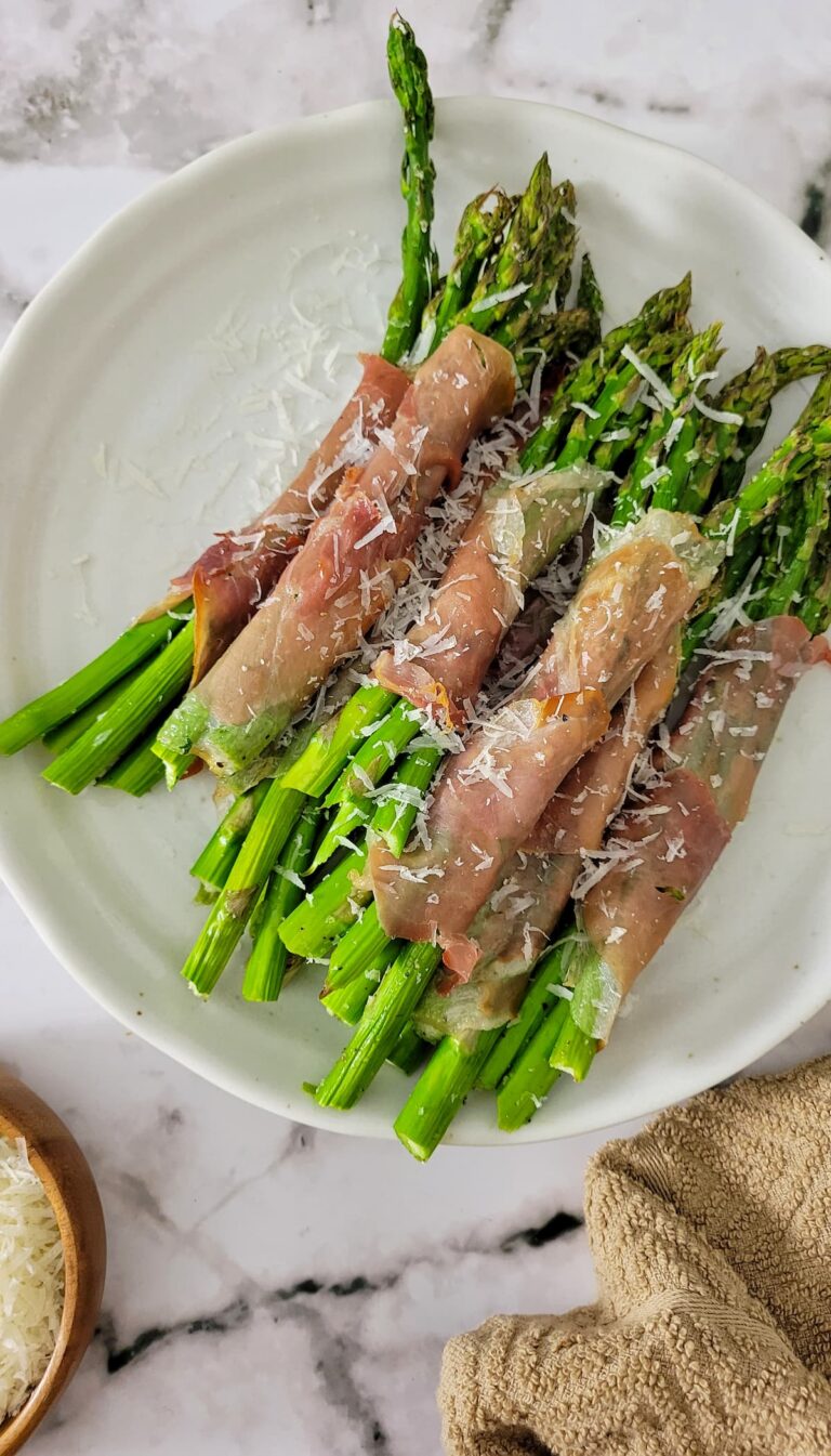 prosciutto wrapped asparagus bundles on a plate garnished with fresh grated parmesan cheese