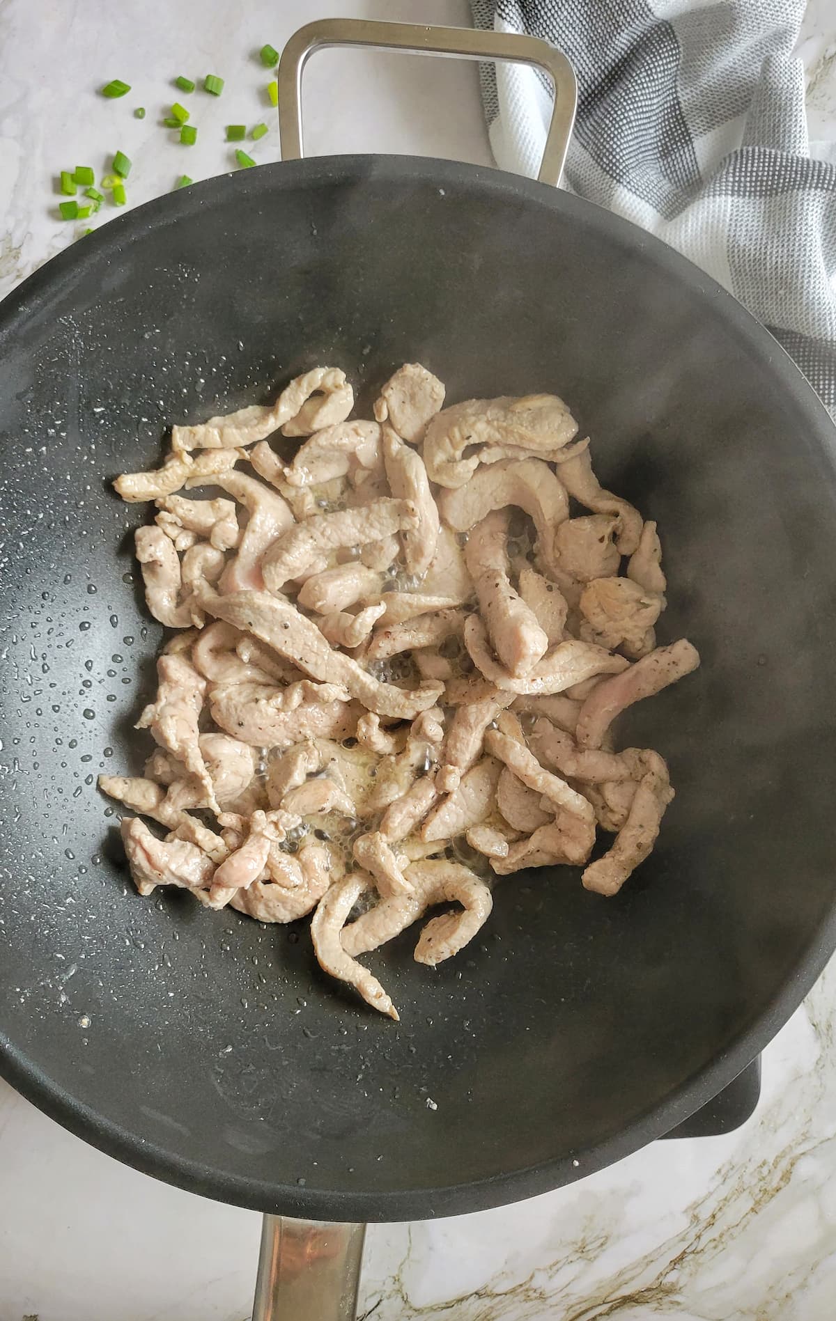 cooked pork strips steaming in a wok