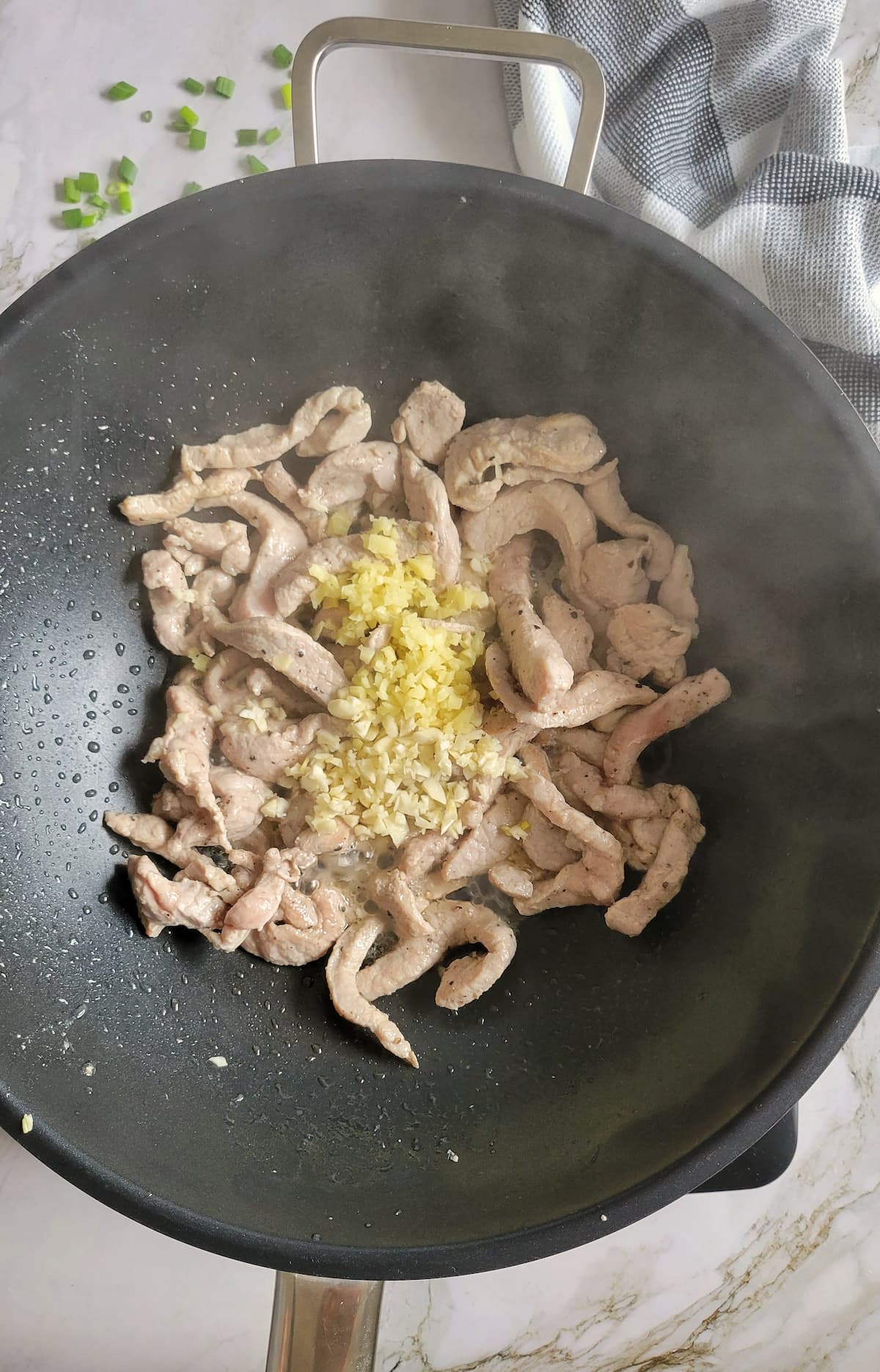 pork strips cooking in a wok with minced garlic and ginger