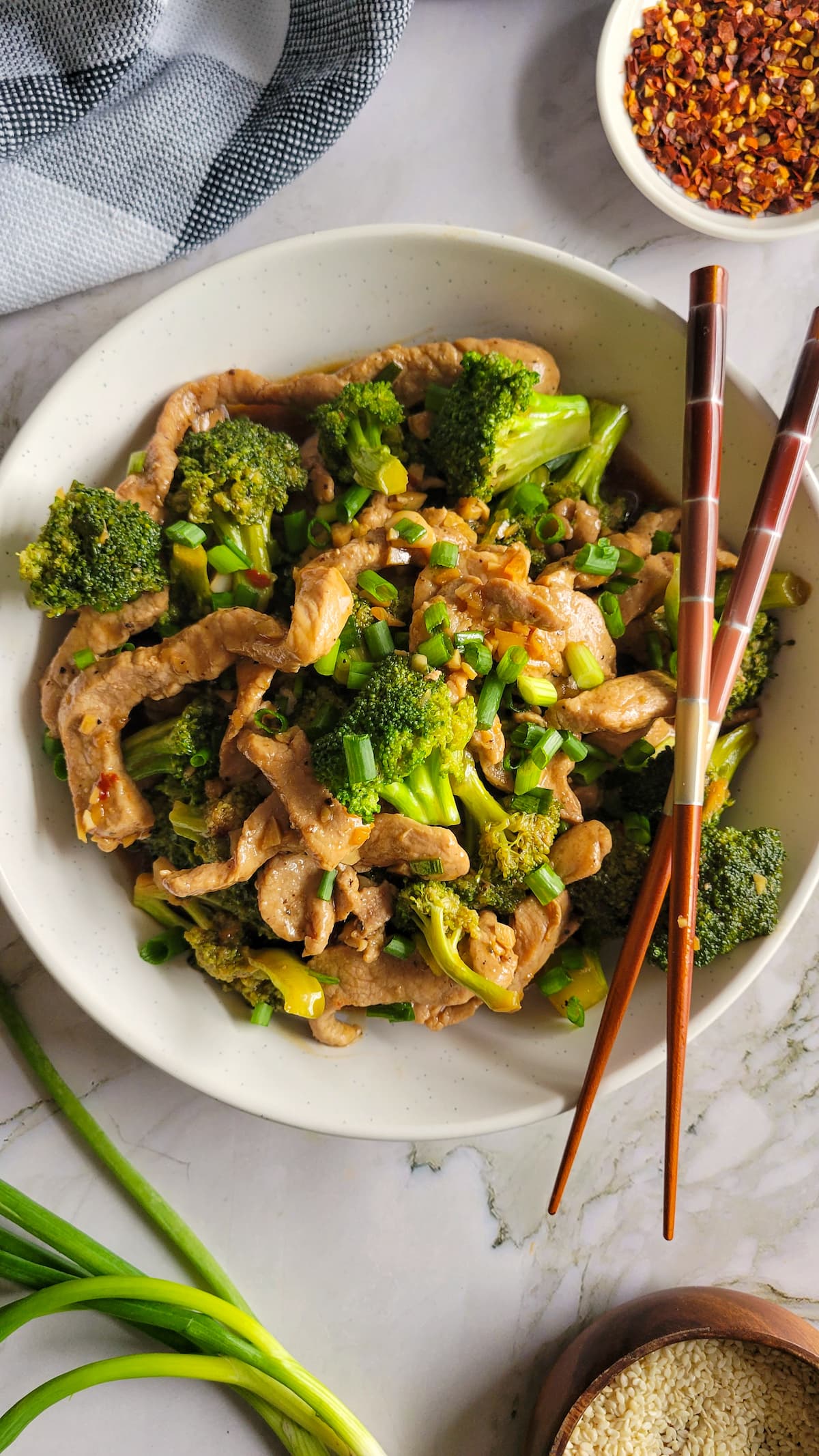 bowl of broccoli, pork and green onions with chopsticks