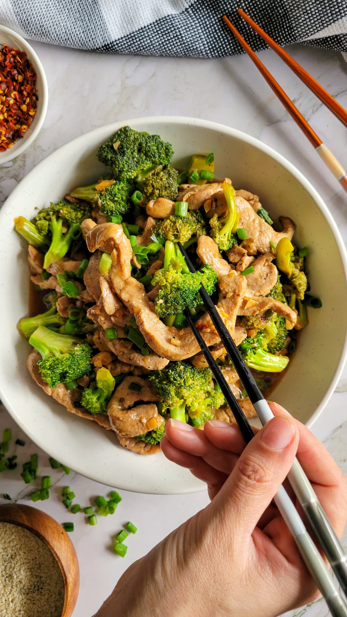 hand with chopsticks in a bowl of stir fried broccoli and pork strips