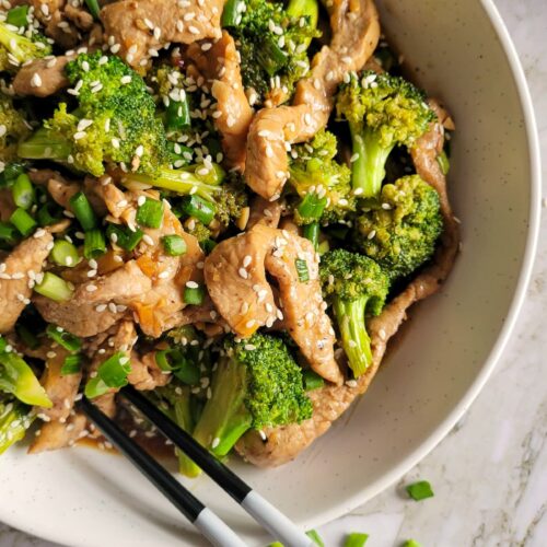 bowl of broccoli and pork strips garnished with green onions and sesame seeds, chopsticks in the bowl