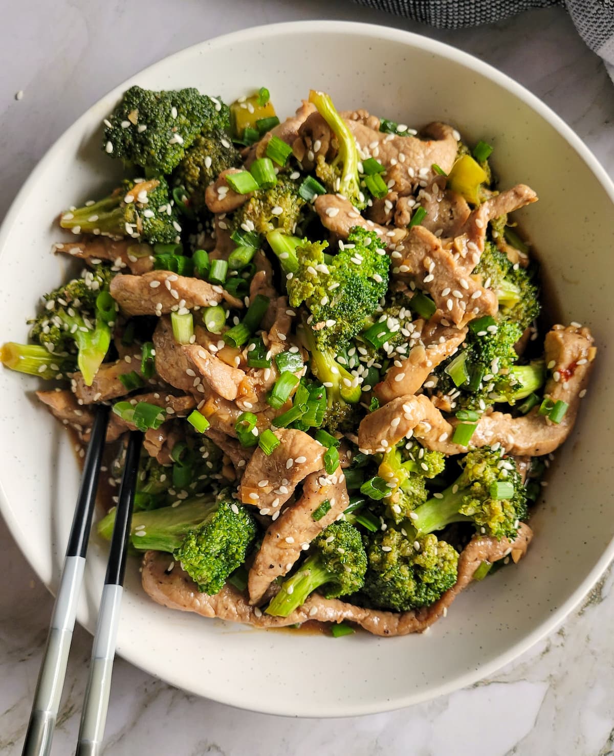 cooked broccoli and pork strips garnished with sesame seeds in a bowl with some chopsticks