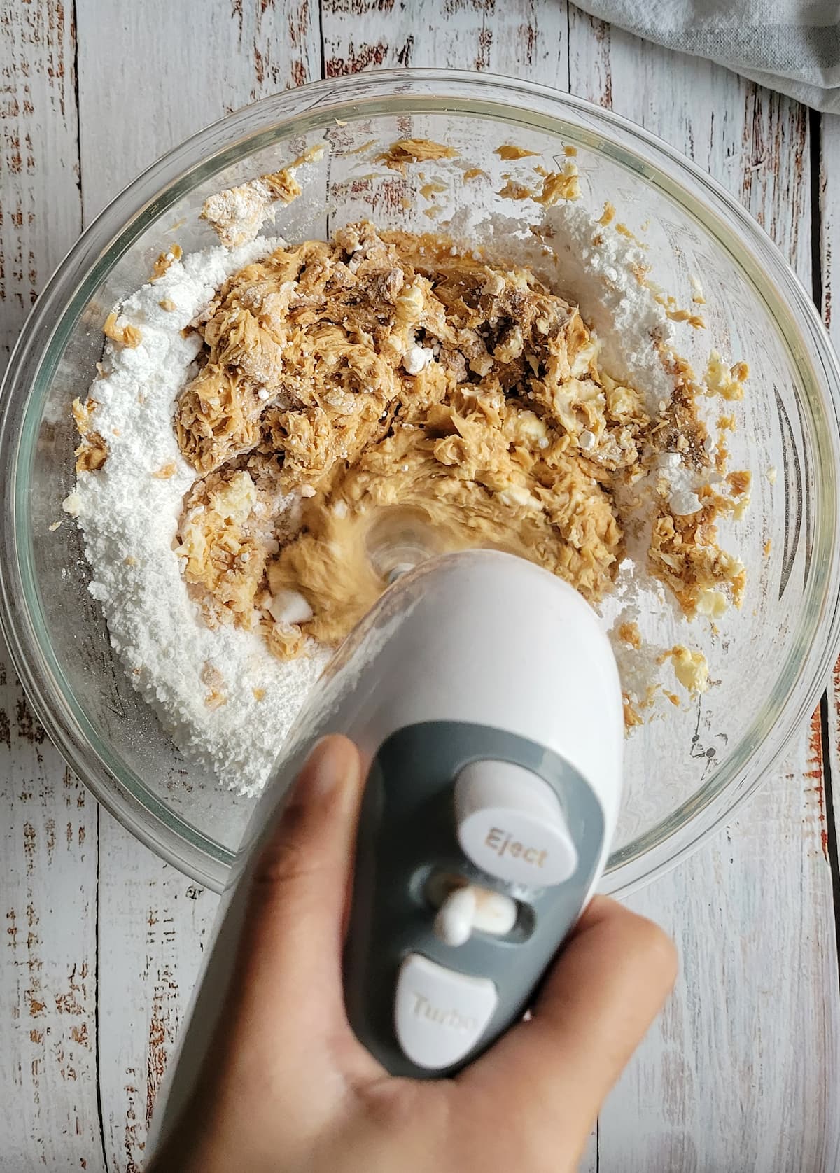 hand with an electric blender blending peanut butter with icing sugar in a bowl