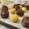 peanut butter balls, some covered in chocolate and some not, on a parchment lined baking sheet, glass of milk in the background