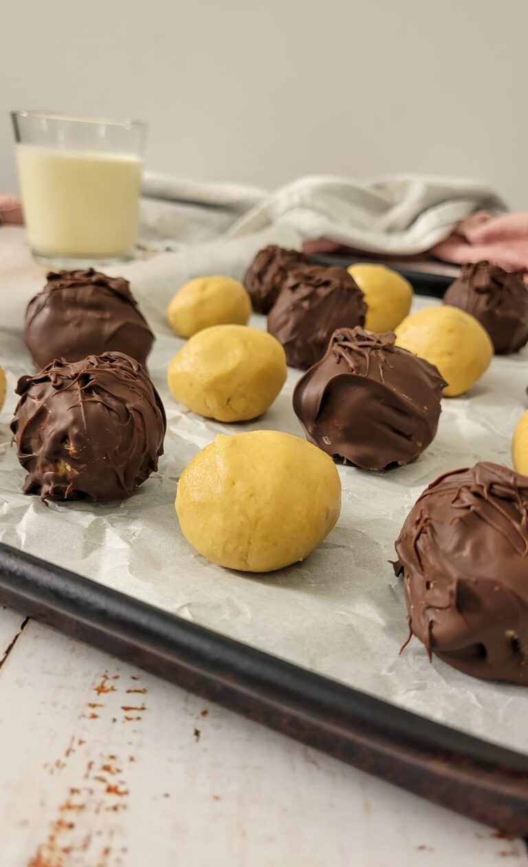 peanut butter balls, some covered in chocolate and some not, on a parchment lined baking sheet, glass of milk in the background