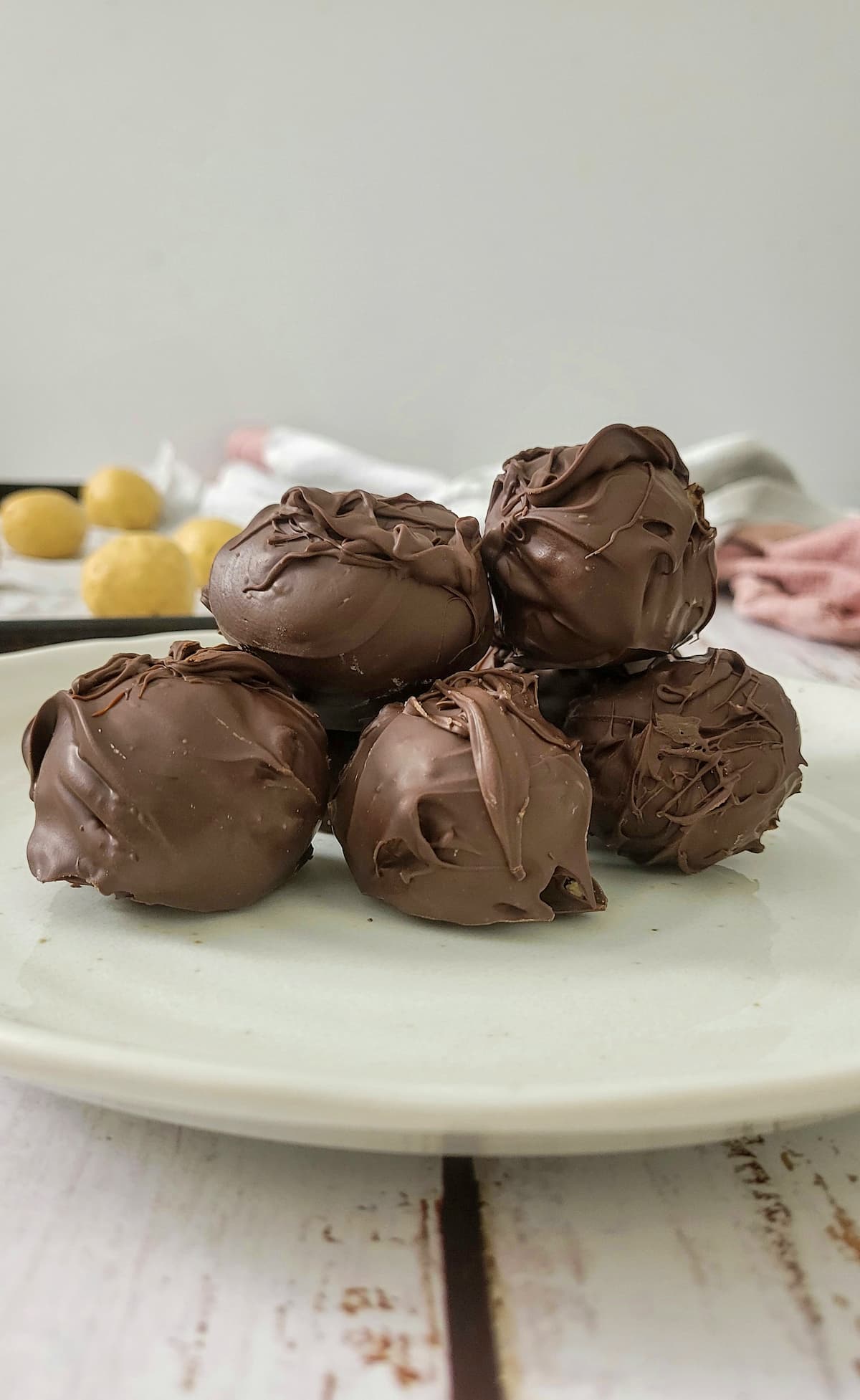 chocolate covered peanut butter balls stacked on a plate, more (not covered in chocolate) in the backgroud