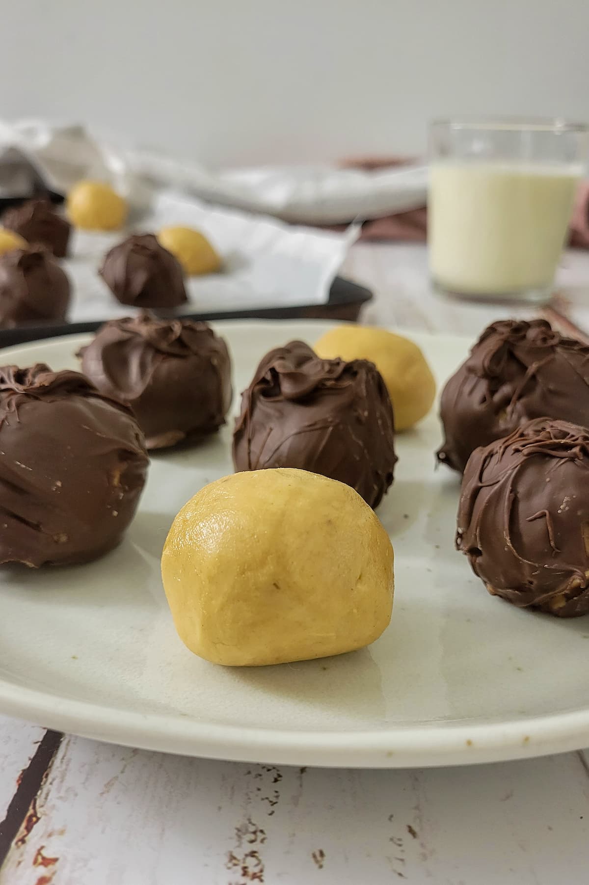 peanut butter balls on a plate and baking sheet, some covered in chocolate and some not, glass of milk in the background