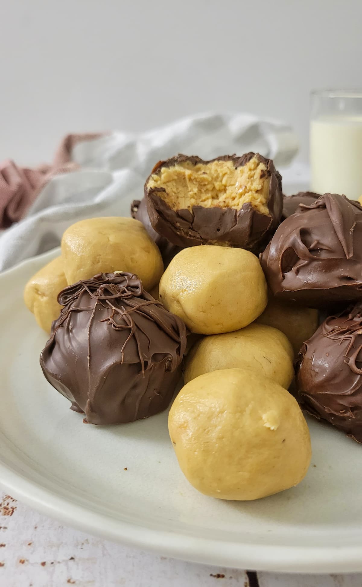 peanut butter balls, some covered in chocolate and some not, stacked on a plate, bite bitten out of the one at the top