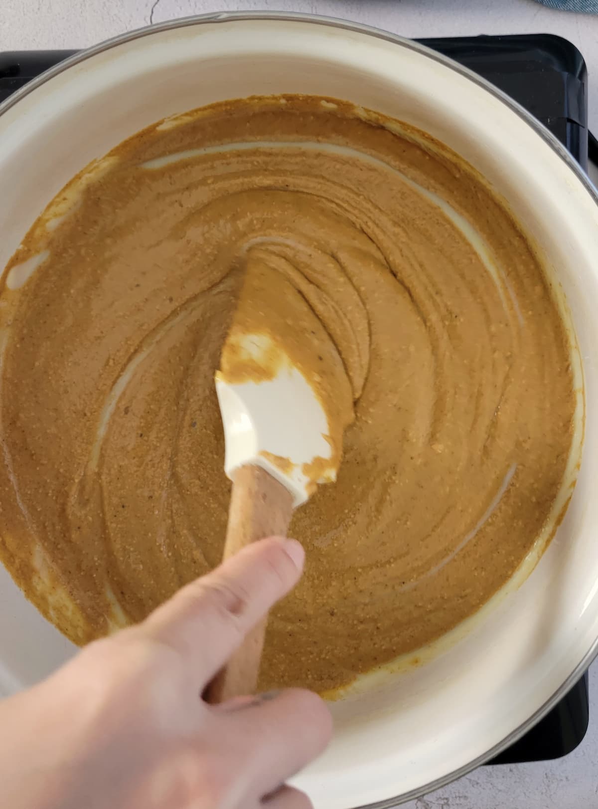 hand with a rubber spatula stirring peanut butter in a pot