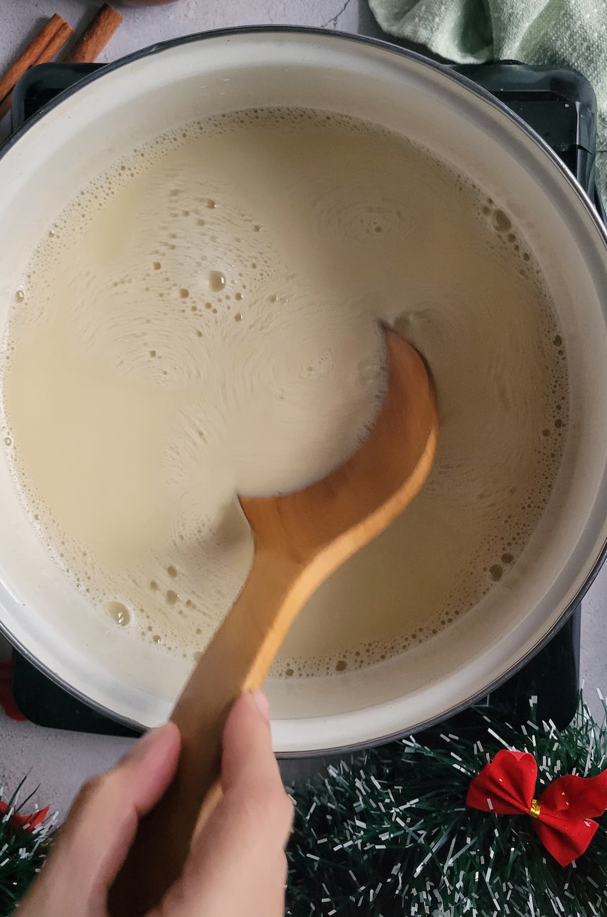 hand with a wooden spoon stirring eggnog in a pot