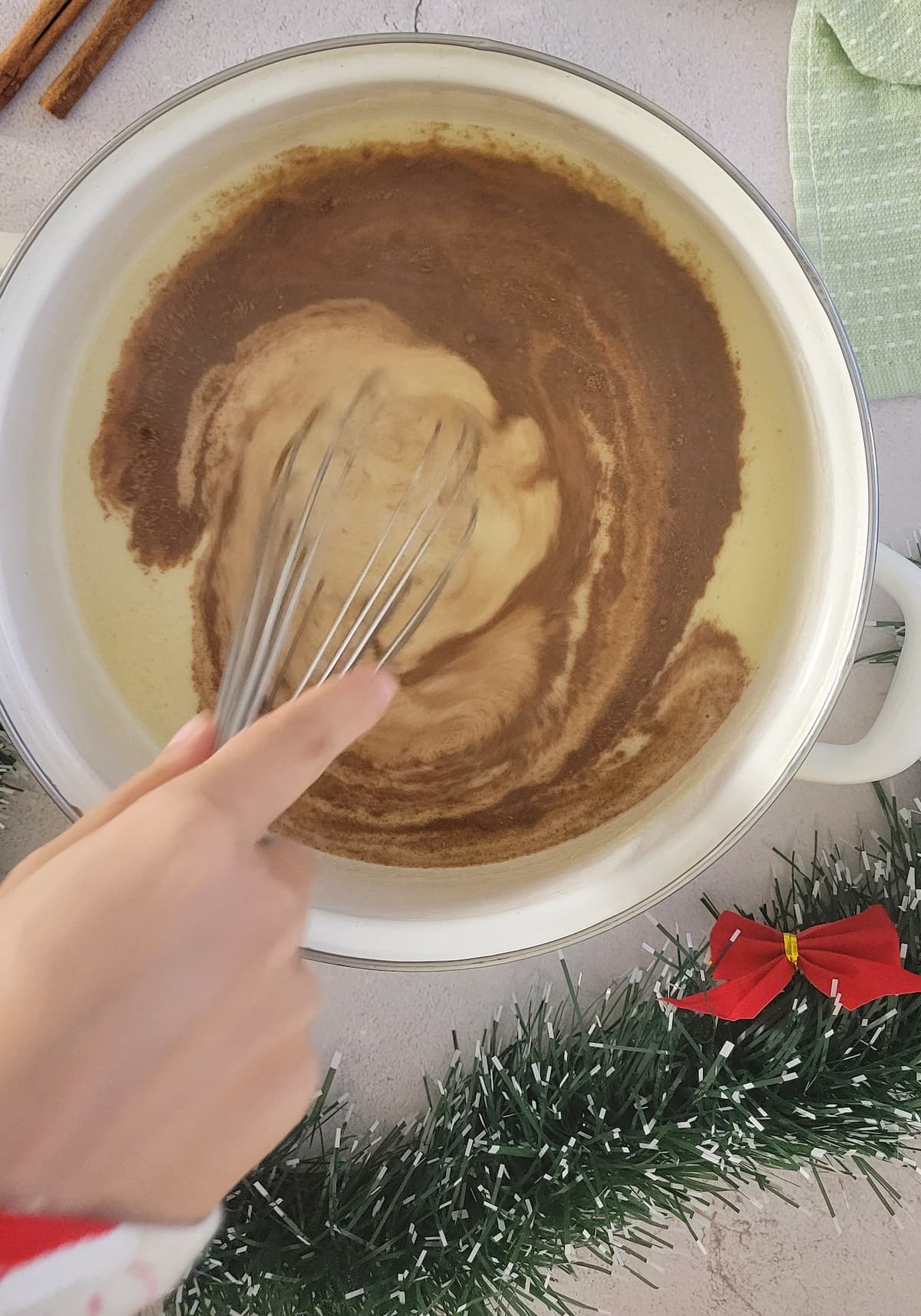 hand with a whisk whisking spices into eggnog in a pot